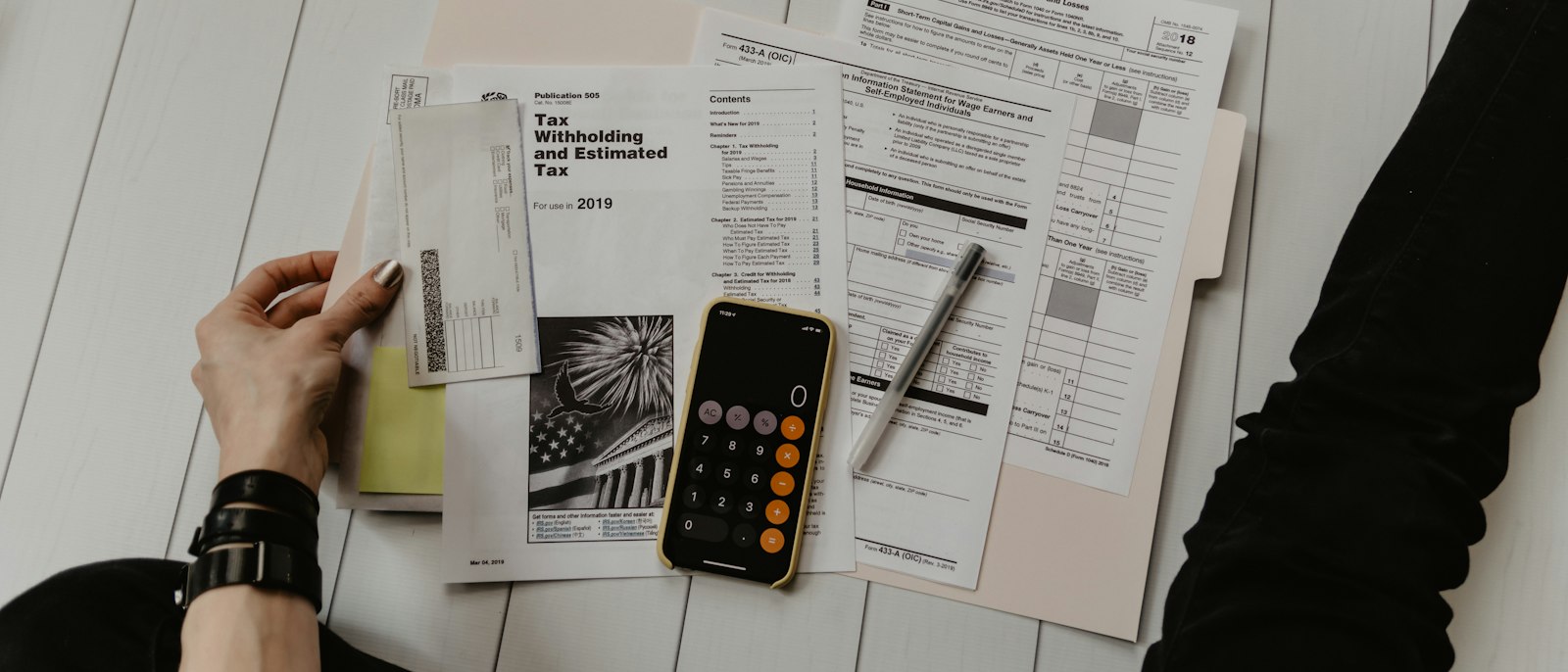IRS tax forms, a calculator and a pen on a white table