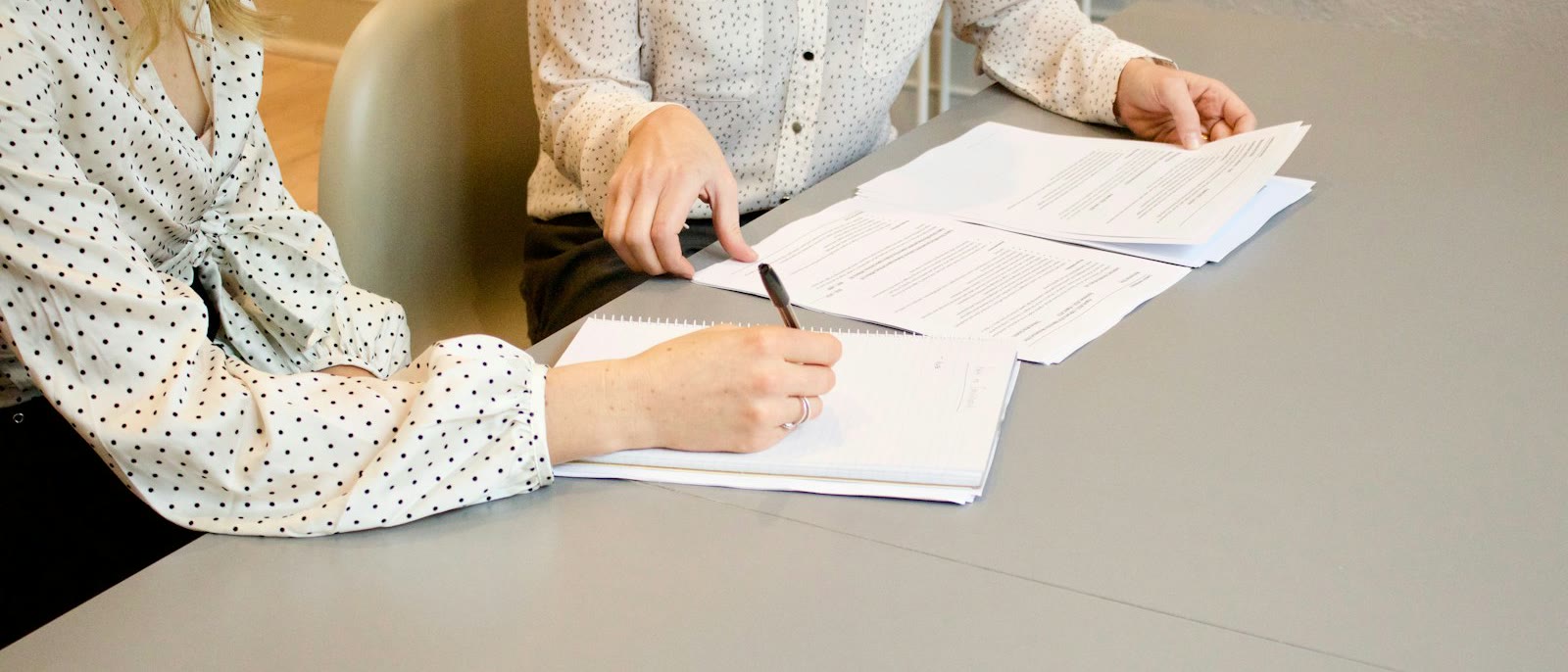 Two people reviewing and signing documents at a grey table