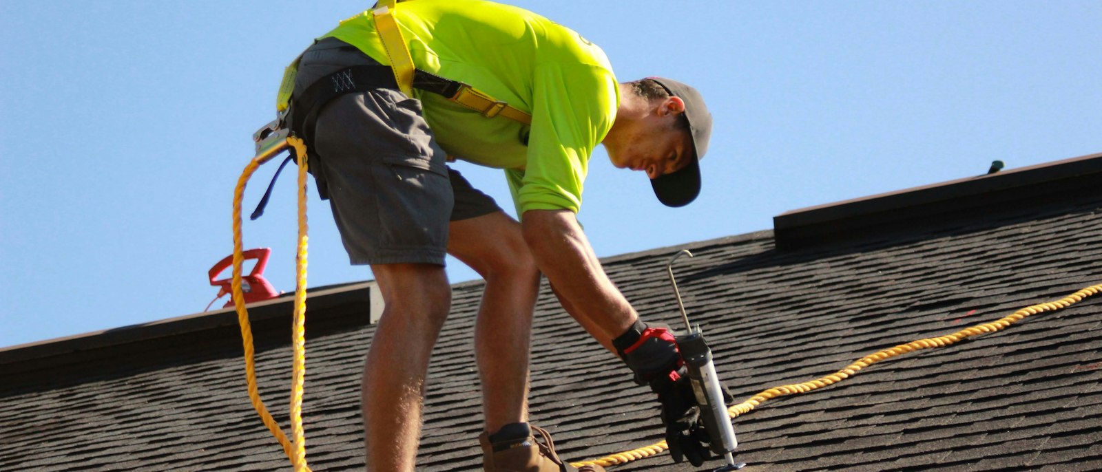 A roofer in a safety harness working on a shingle roof